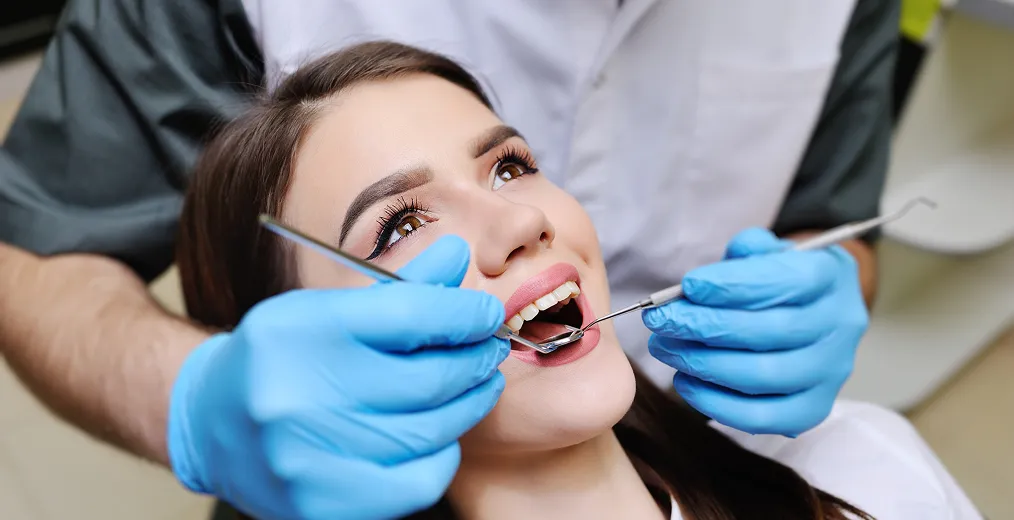 A close view of a smiling woman's teeth being checked with a dental mirror and probe