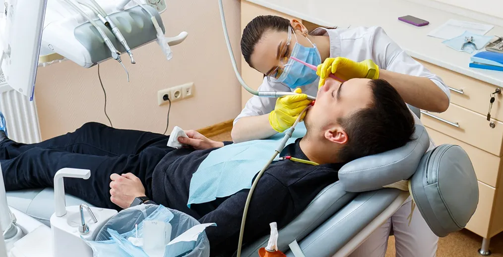 A dentist and an assistant treat a man lying back in a dental chair